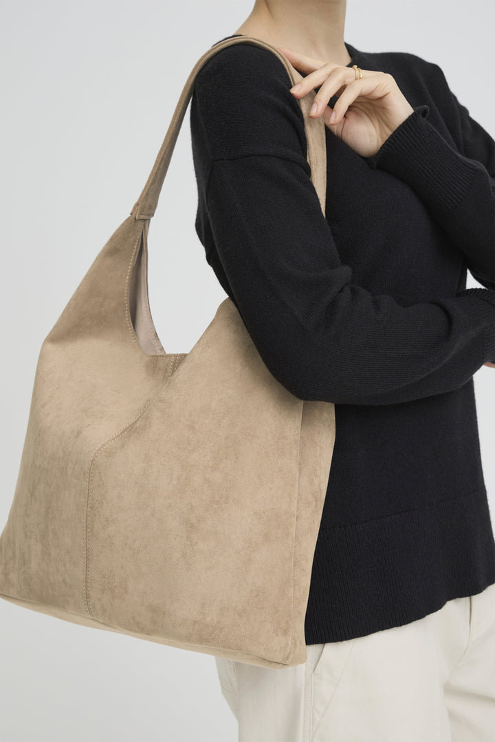 Person holding a beige handbag against a plain background