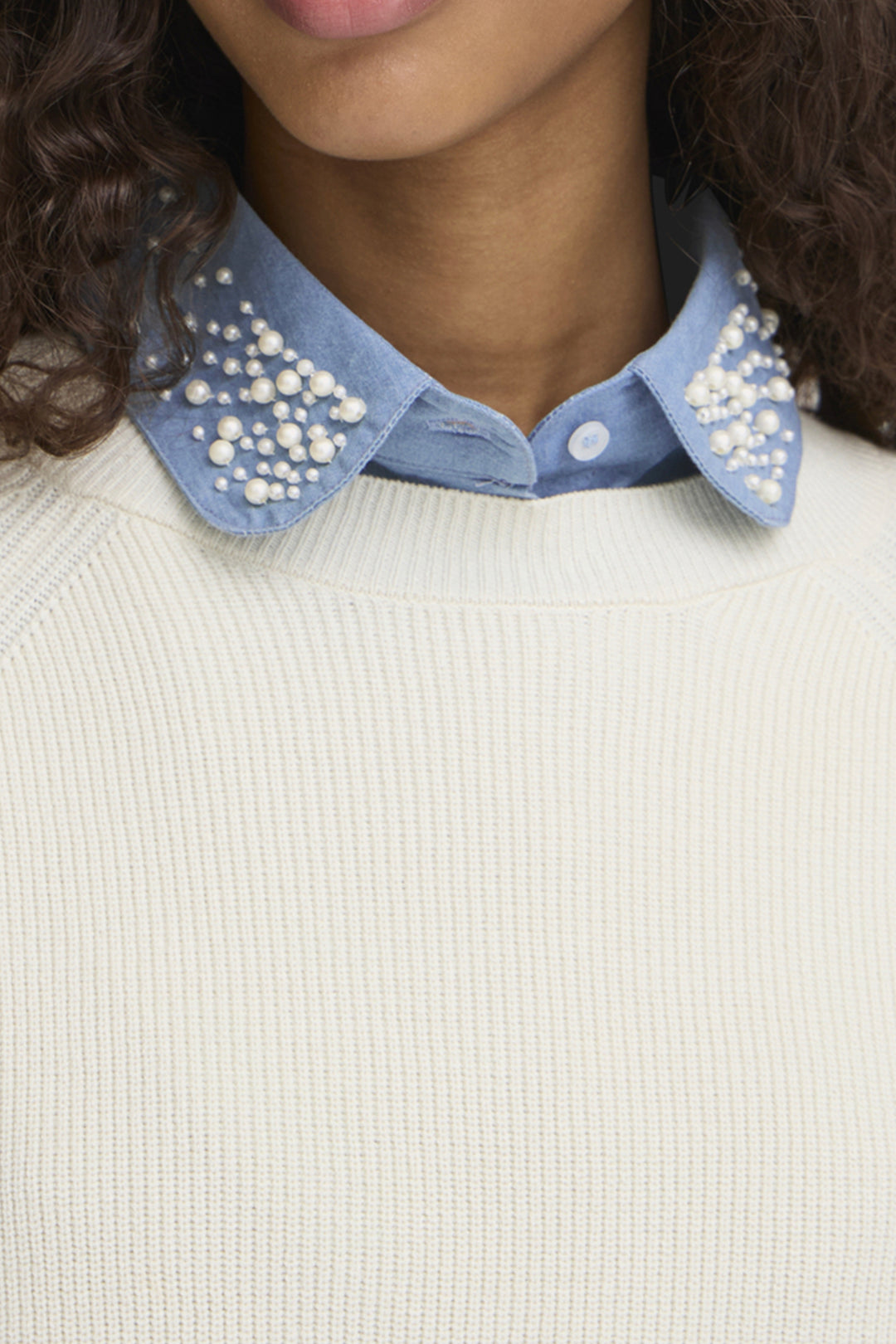 Close-up of a person wearing a white sweater with a blue collar accessory featuring pearl embellishments.