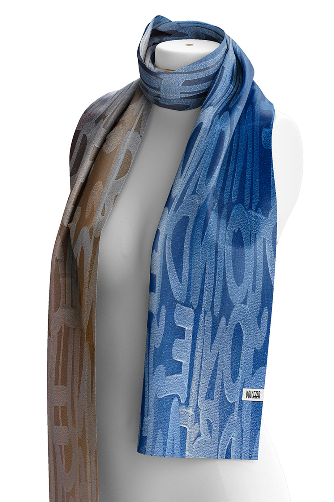 A blue and brown patterned scarf draped on a white mannequin torso against a white background. The scarf features a blue side with light blue abstract lettering and a brown side with beige and brown abstract lettering.