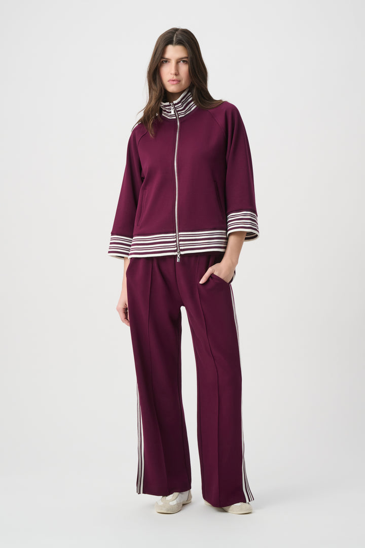 Woman wearing a purple tracksuit with white stripes on a white background
