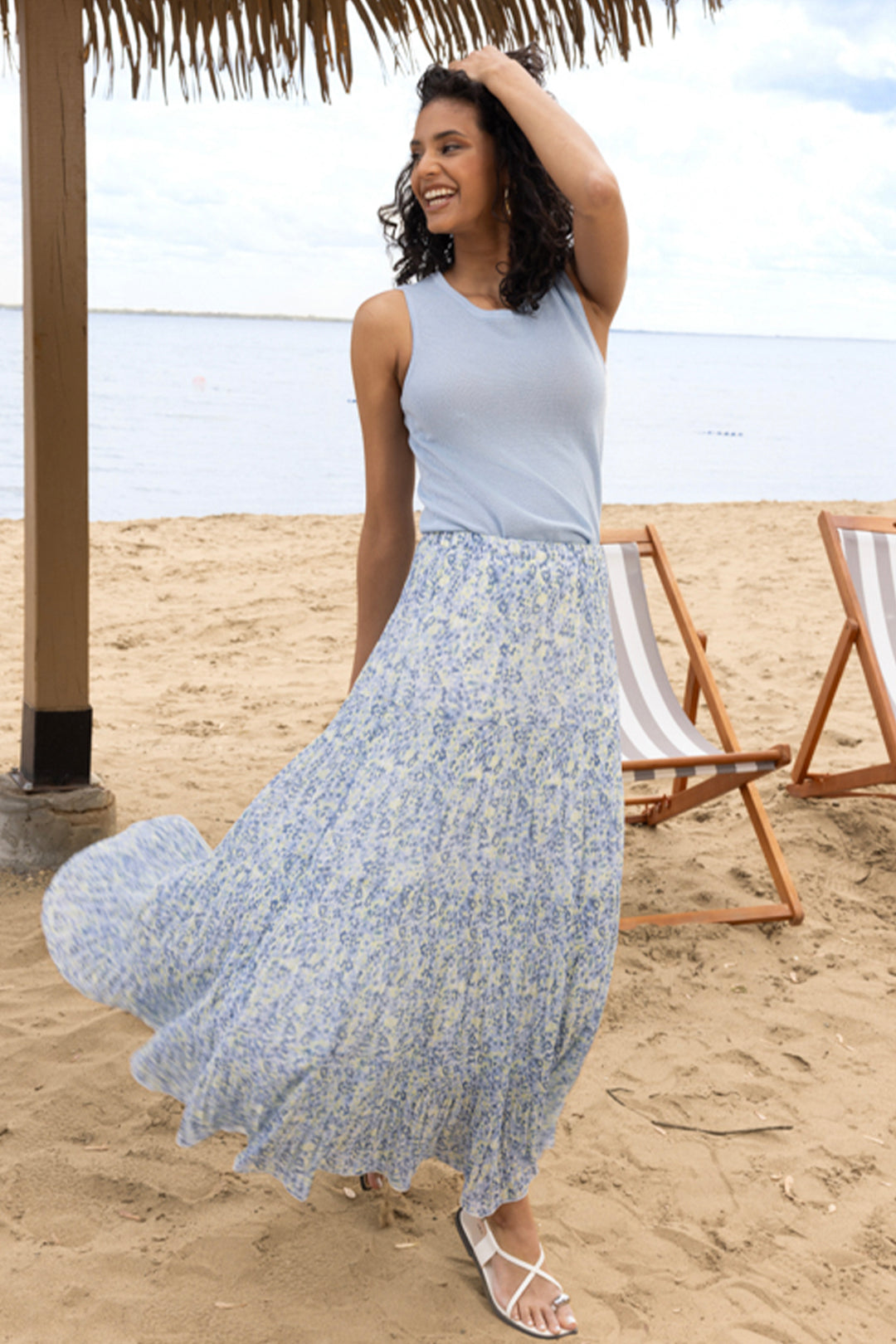 Woman in a floral skirt standing on a sandy beach with ocean view.