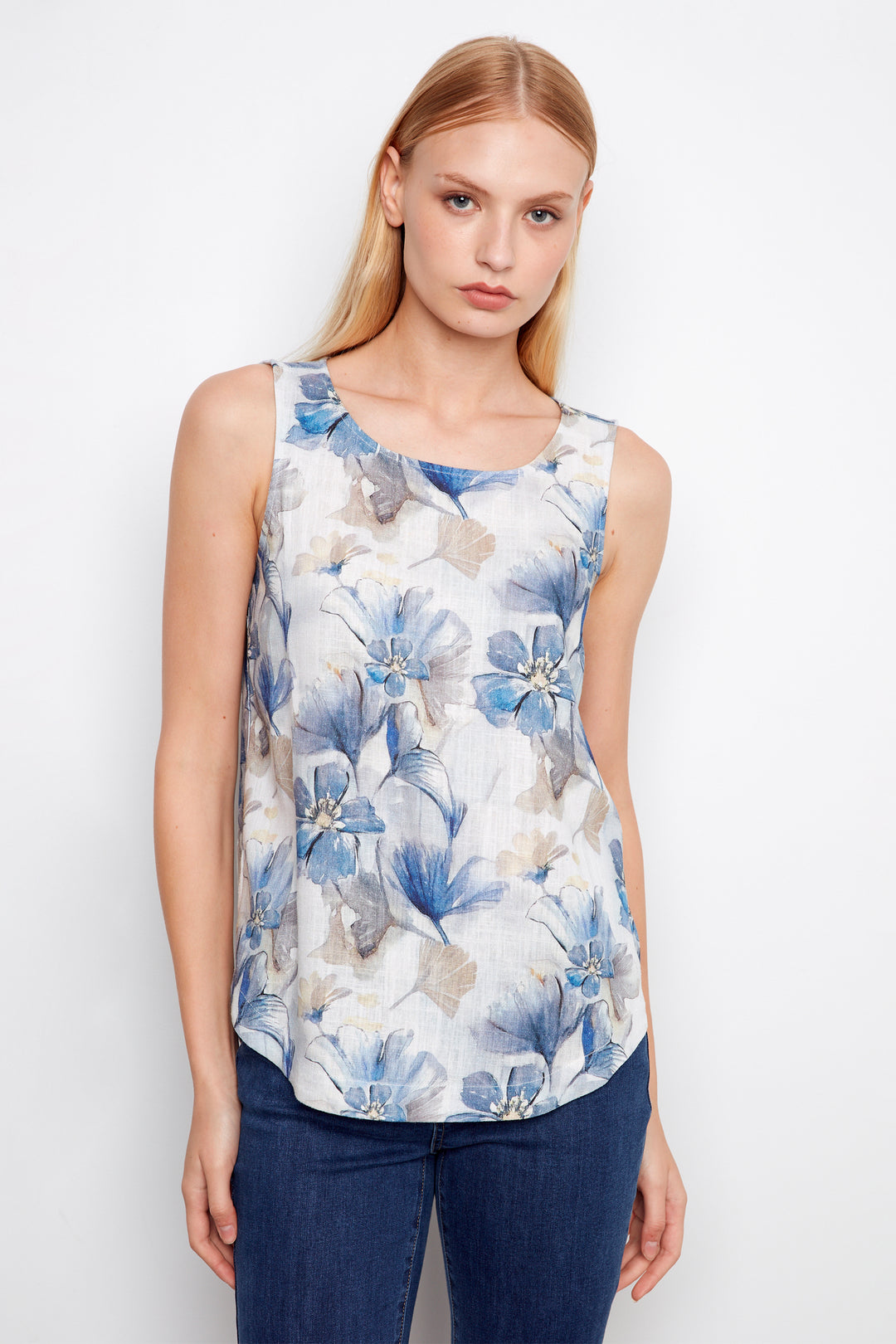 Woman wearing a sleeveless floral top with blue and white flowers on a plain background
