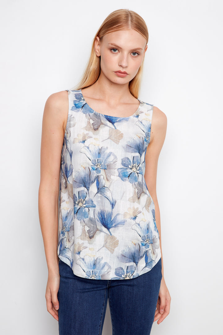 Woman wearing a sleeveless floral top with blue and white flowers on a plain background