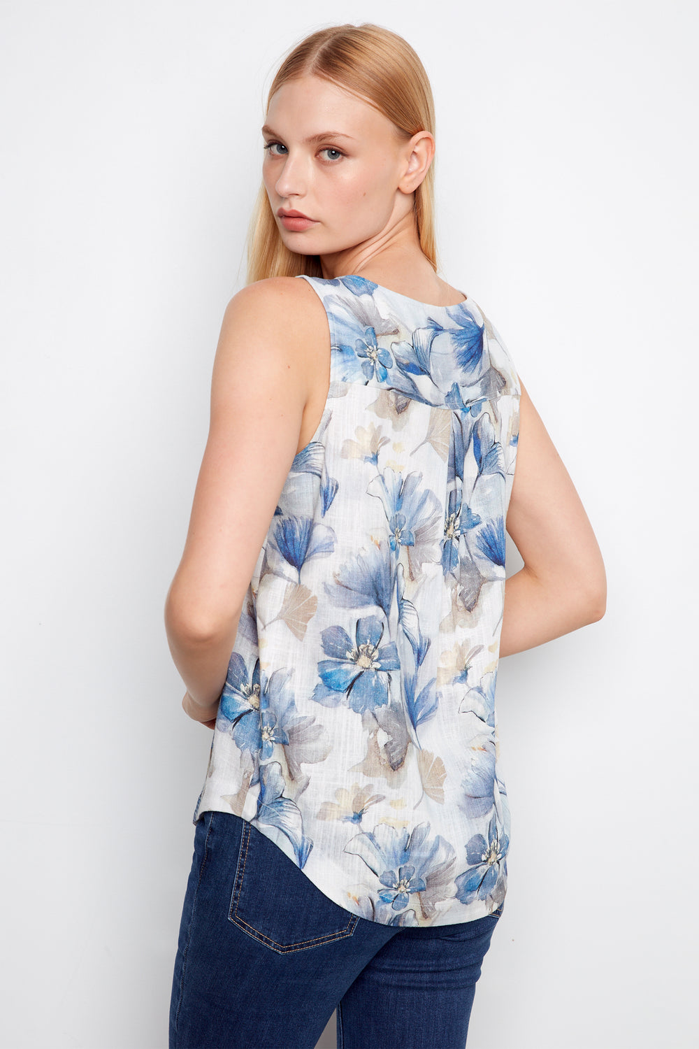 Woman wearing a sleeveless floral top with blue and white flowers on a plain background
