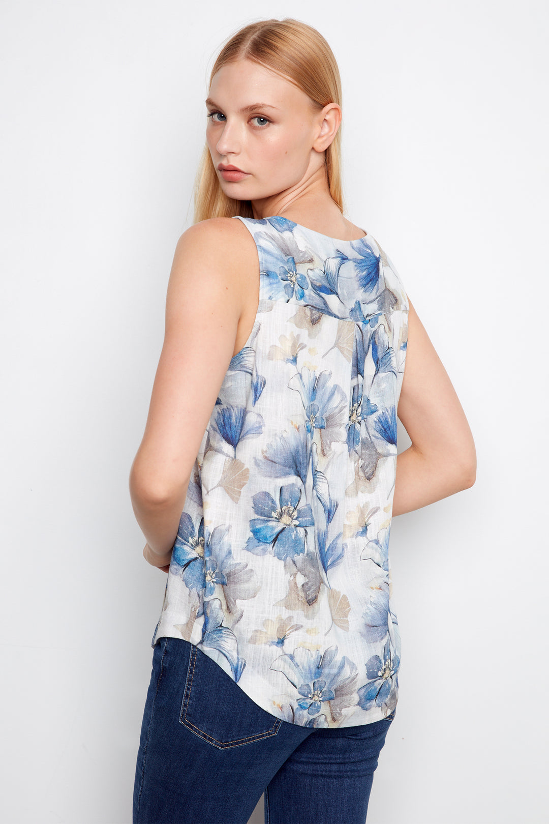 Woman wearing a sleeveless floral top with blue and white flowers on a plain background