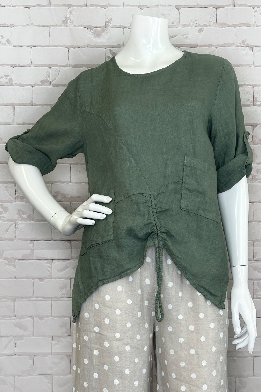 Cherishh Spring 2024 With side hem cuts, a round neck and two front pockets, this top is both functional and fashionable. The button roll-up sleeves and ruched front hem with drawstring add a playful touch.