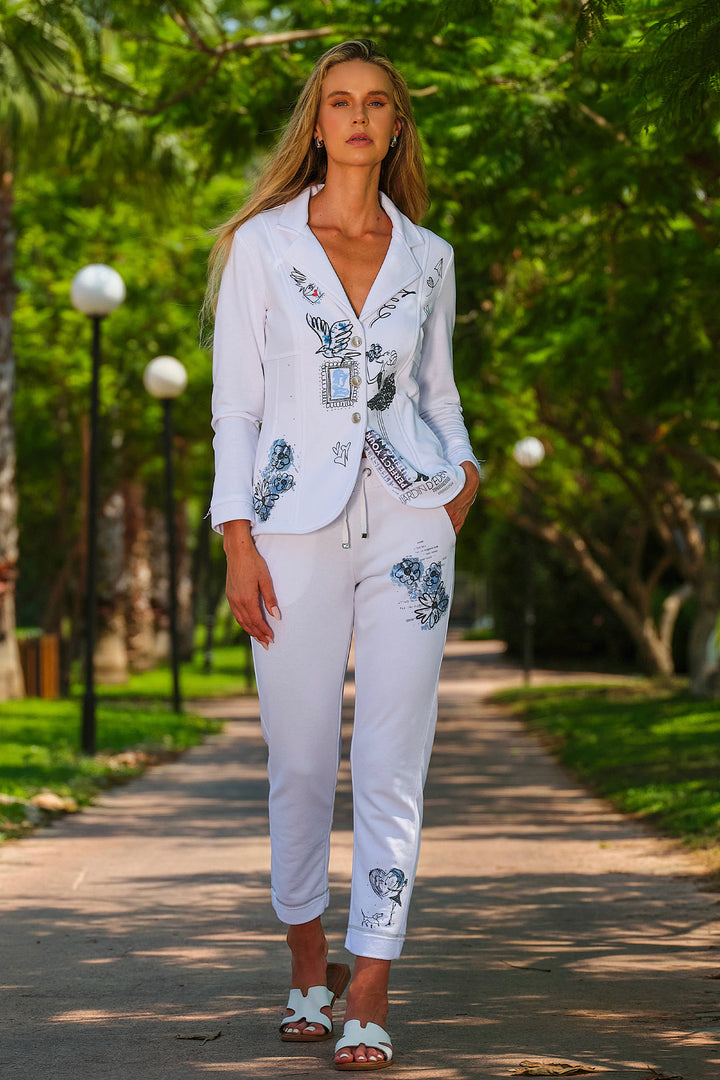 Woman in a white outfit with floral embroidery walking on a path in a park.
