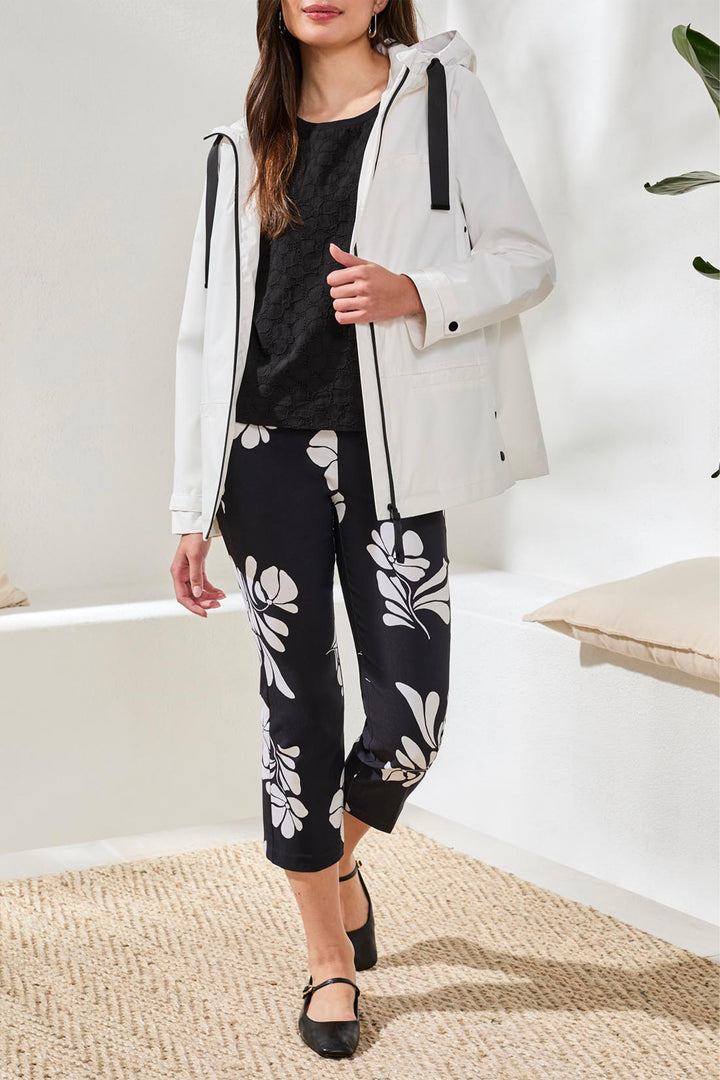 Woman wearing a white coat, black top, and black pants with white patterns indoors.